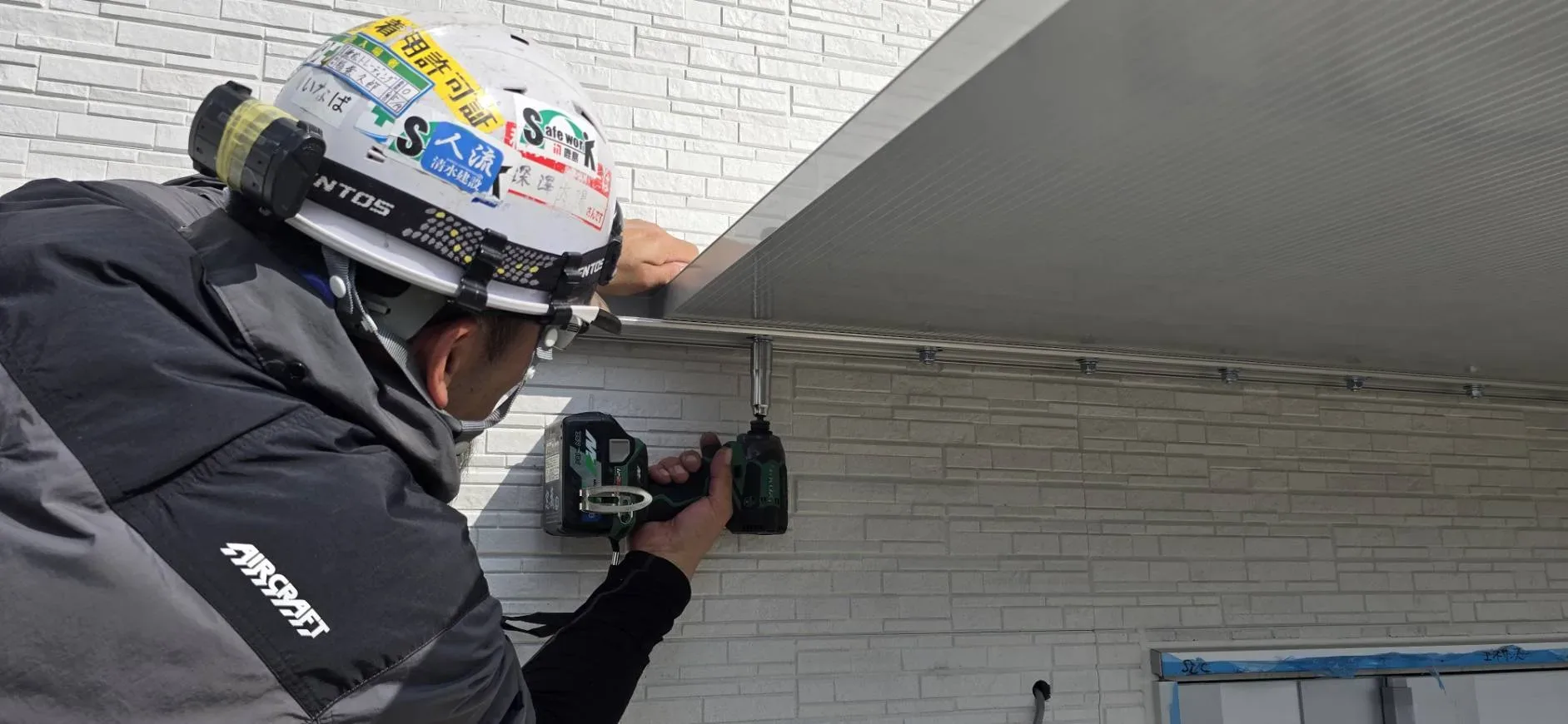 外壁にアルミ庇を取り付け、電動工具で固定する職人