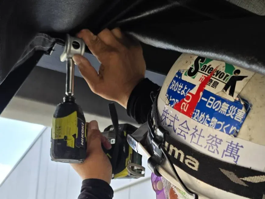 天井の防鳥網の金物を電動工具で固定する窓萬の職人